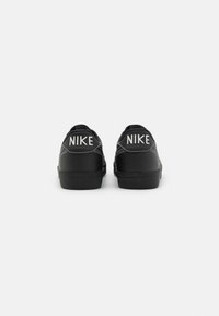 Fekete Nike sportcipők sima bőr felülettel, kontrasztos fehér logóval a saroknál, valamint texturált fekete gumitalppal.