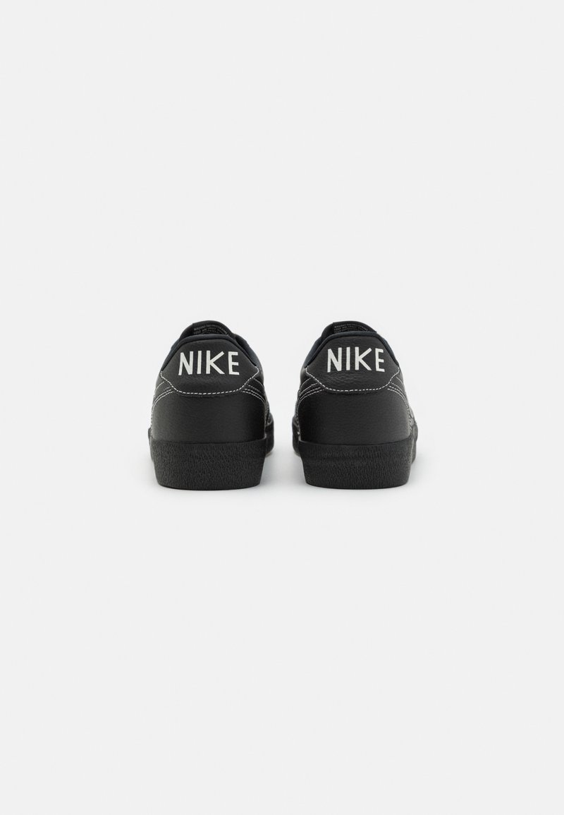 Zapatillas Nike negras con una superficie de cuero suave, que cuentan con texto de logo blanco en contraste en el talón y una suela de goma negra texturizada.