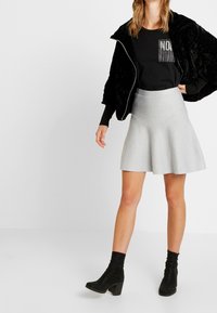 Black plush bomber jacket over a black t-shirt with metallic detail, paired with a silver flared skirt and black heeled ankle boots.