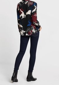 Koszula z długim rękawem o czarnej bazie, z żywym wzorem kwiatowym w kolorach czerwonym, niebieskim i kremowym. Zestawiona z ciemnoniebieskimi dżinsami skinny oraz botkami za kostkę.