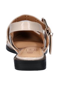 Beige gepatenteerde leren sandaal met een platte zwarte zool, voorzien van een gespstrap en een open ontwerp, dat een gladde beige binnenkant blootlegt met details van de voetbed.