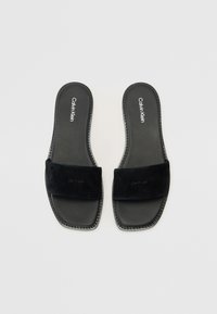 Sorte sandaler med glidesåle som har en myk semsket stropp, glatt lærsåle og sømfinerte kanter. Merkevare på stroppen.