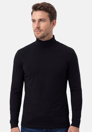 Ung mand med lyst brunt hår iført en sort langærmet rullekrave, der kigger let til siden mod en ensfarvet baggrund.