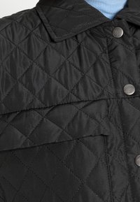 Giacca nera trapuntata con colletto, caratterizzata da un motivo a rombi, bottoni a pressione argentati e una texture liscia.