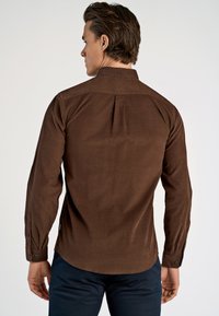 Bruin langarmshirt met een gestructureerde kraag, knoopmanchetten en een textuurstof. Kenmerkt zich door een plooi aan de achterkant en een afgeronde zoom.