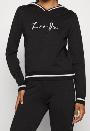 Black hooded sweatshirt with a shimmery texture, featuring a white cursive logo and striped ribbed cuffs and hem, providing a fitted design.