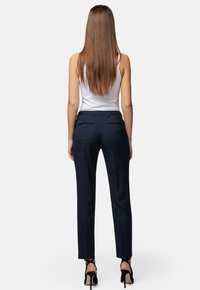 Granatowe spodnie taliowane o prostym kroju, z tylnymi kieszeniami i dwiema guzikami. Noszone z białym tank topem i czarnymi szpilkami.