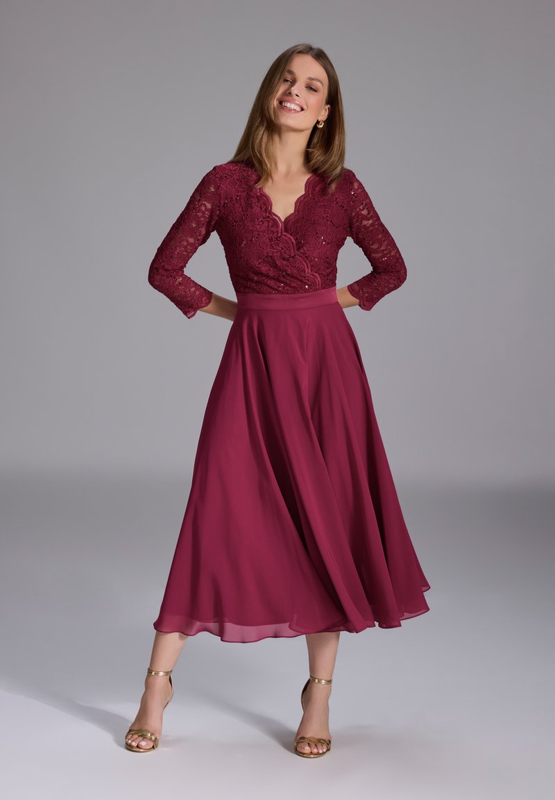 Burgundy lace dress with a scalloped neckline and three-quarter sleeves; flowing A-line chiffon skirt and golden strappy heels.