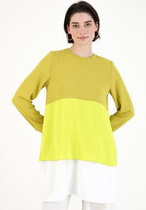Maglietta a maniche lunghe con scollatura rotonda, caratterizzata da un design a blocchi di colore in verde olivastro e giallo fluorescente, sovrapposta a una sezione inferiore bianca.