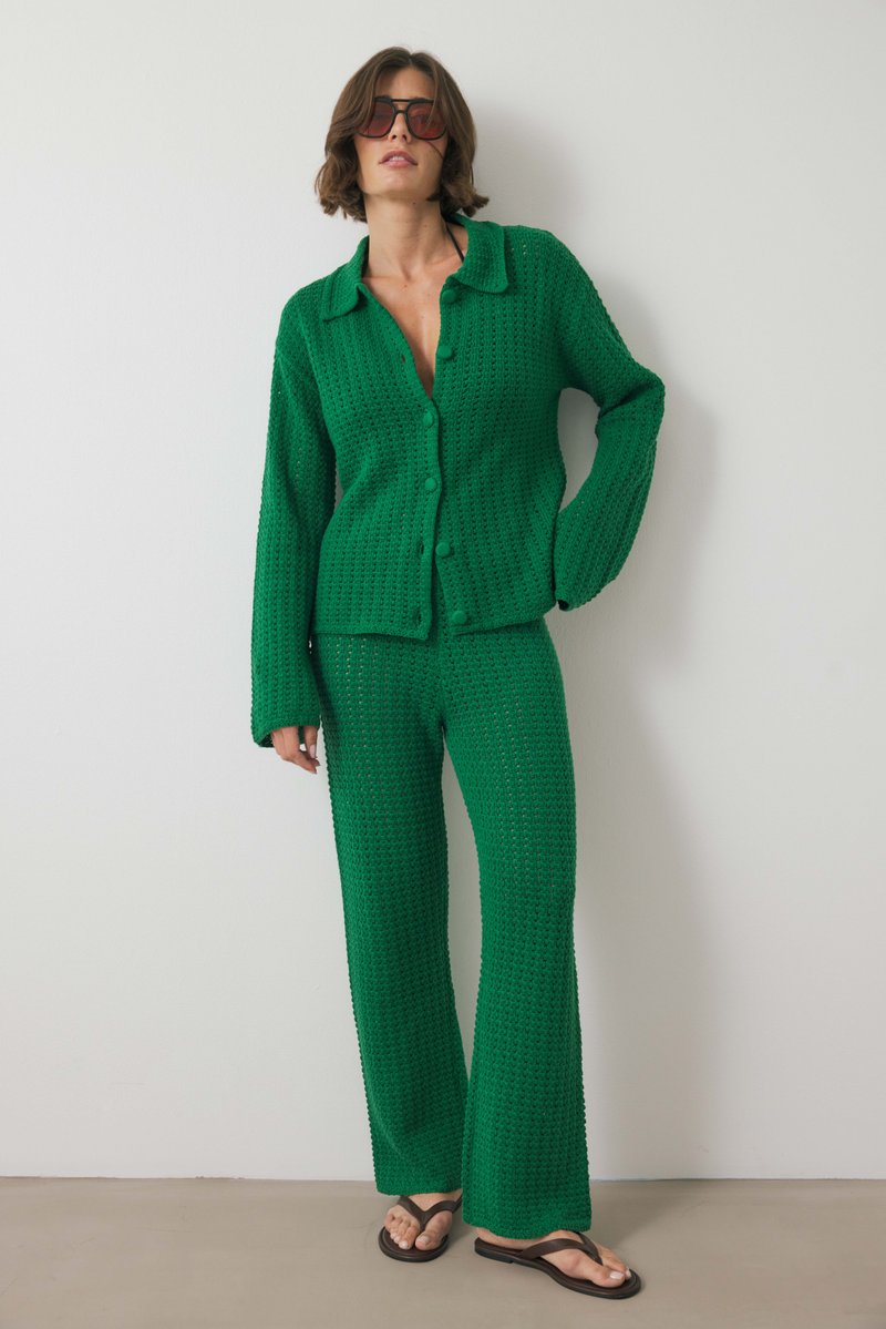 Zaļa adīta kardigāna ar pogām un garām piedurknēm, apvienota ar atbilstošām platām biksēm. Materiālam ir teksturēts, atvērts auduma dizains.