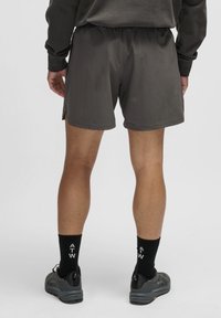 Grå sportshorts med elastisk midja, sidofåror och en mjuk textur. Bärs med svarta strumpor med vit text och mörka skor.