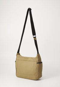 Khaki shoulder bag with a soft texture, rectangular shape, adjustable black strap, and front zipper pocket. Side pockets for additional storage.