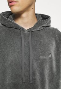 Sudadera con capucha gris de acabado texturizado, con cordones ajustables y un pequeño logotipo bordado en el lado izquierdo del pecho.