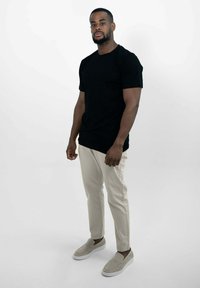 Zwarte korte mouwen t-shirt gecombineerd met lichtbeige slim-fit broek en lichtgrijze instapschoenen. Eenvoudig ontwerp, gladde stofafwerking.