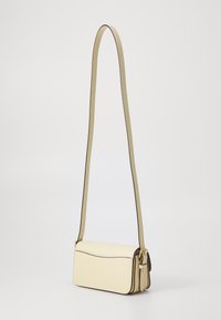 Ādas crossbody soma bālā dzeltenā krāsā ar plakanisku taisnstūra formas dizainu, kontrastējošu tumšu apdari un regulējamu siksnu.