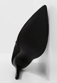 Chaussure talon aiguilles en daim noir vue en angle, avec un bout pointu et une semelle texturée, sur un fond blanc d'angle.