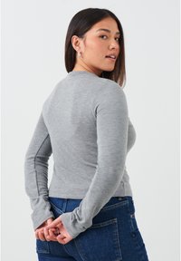 Grijze longsleeve top gemaakt van zachte stof, met een fitted ontwerp en een ronde hals; gecombineerd met donkere blauwe jeans.