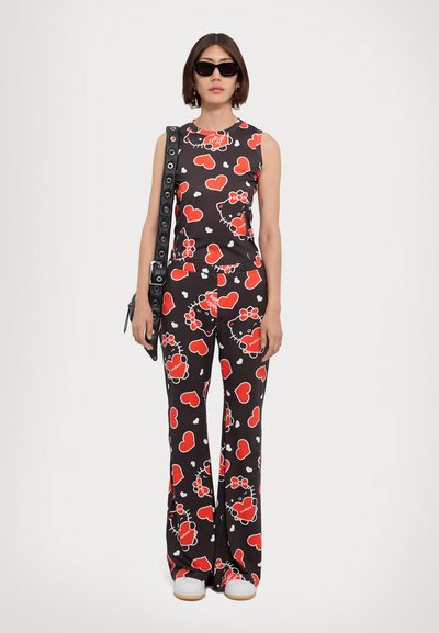 Black sleeveless jumpsuit with red and white heart and Hello Kitty patterns. Model wears sunglasses and a black bag with silver hardware.