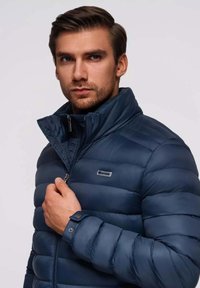 Marineblaue Steppjacke mit Stehkragen, auffälligem Reißverschluss und gerippten Ärmelabschlüssen. Leicht und gesteppter Schnitt mit Logo.
