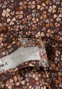 Tissu marron avec un motif floral multicolore, présentant des fermetures à boutons-pression sur un bord replié révélant une doublure intérieure blanche.