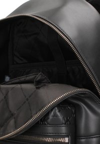 Interno dello zaino in pelle nera con tasca con cerniera, fodera in tessuto con motivo a logo ripetuto e cinghie elastiche per l'organizzazione.