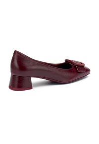 Décolleté in pelle bordeaux con tacco basso e dettaglio a fibbia quadrata sulla punta, vista laterale angolata su sfondo bianco.