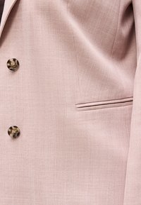 Lys rosa blazer med to knapper i skilpaddeskall og en horisontal spisslomme på høyre side.