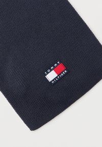 Πλεκτό ύφασμα σε ναυτικό μπλε με ένα ορθογώνιο έμβλημα Tommy Hilfiger που εμφανίζει τα χρώματα κόκκινο, λευκό και μπλε.