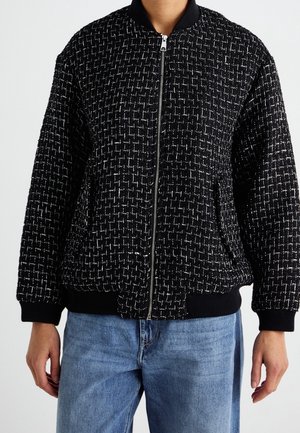 Sort og hvid ternet lynlåstrøje med ribbet krave, manchetter og kant, båret sammen med lyseblå jeans.