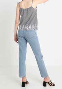 Black and white gingham camisole with lace trim, paired with light blue high-waisted jeans featuring a distressed knee and black strappy heels.