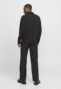 Zwarte langemouwen shirt met een textuurafwerking, voorzien van een kraag en een rechte snit. Gecombineerd met op maat gemaakte zwarte broeken en zwarte schoenen.