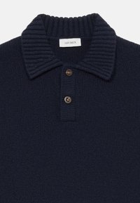 Dunkelblauer Strickpullover mit einem gerippten Kragen, zwei braunen Knöpfen und einem "LES DEUX"-Etikett im Kragen.