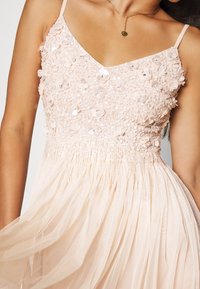 Ein hellrosa Kleid mit einem taillierten, mit Pailletten verzierten Oberteil, das mit floralen Applikationen geschmückt ist, und einem fließenden, transparenten Rock mit geraffter Textur.