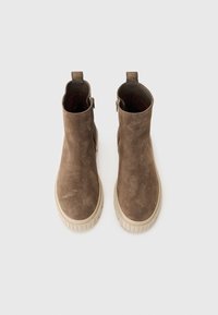 Bruine suède enkelboots met een dikke crèmekleurige zool, voorzien van een rits aan de zijkant en trekriemen voor gemakkelijk aantrekken. Glad textuur.