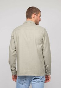 Chemise à manches longues gris clair avec une texture douce, poignets boutonnés et col classique, présentée de dos. Coupe décontractée, portée avec un jean bleu.
