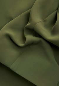 Gros plan d'un tissu côtelé vert olive avec une couture visible et des plis doux créant une texture et des ombres délicates.