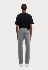 T-shirt noir à motif avec une coupe décontractée, associé à un jean gris à jambe droite avec poches arrière et une petite étiquette de marque. Baskets blanches.