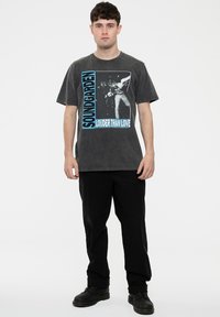 Gray cotton t-shirt featuring a graphic print with "Soundgarden" and "Louder Than Love" text in blue, paired with black pants and boots.