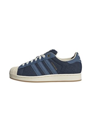 Low-top Adidas Superstar sneaker in donker- en lichtblauw denim met een witte rubberen neus, witte veters en een beige zool.