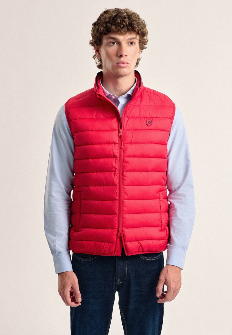 Chaleco acolchado rojo con cuello alto, cierre de cremallera y dos bolsillos laterales. Fabricado con material ligero, presenta costuras horizontales.