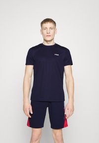 Conjunto atlético de FILA que incluye una camiseta de manga corta azul marino y pantalones cortos azul marino con acentos rojos en los laterales, fabricado en tejido ligero.