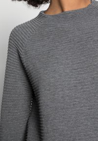 Pull gris côtelé avec un col montant et un motif texturé. Le tissu semble doux avec une légère élasticité et une coupe ajustée aux épaules.
