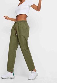 Vihreät pellavaiset jogger-housut, joissa on joustava vyötärönauha ja nyöri, sivutaskut ja rento istuvuus. Yhdistetty valkoisiin tennareihin.