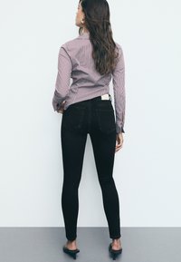 Črne ožje kavbojke z visokim pasom, dvema zadnjima žepoma in usnjeno oznako. V kombinaciji z slikastim srajčnim zgornjim delom. Gladka tekstura.