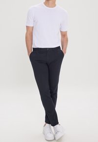 T-shirt blanche à col rond et manches courtes associée à un pantalon slim-fit marine foncé et des baskets blanches, sur fond clair.