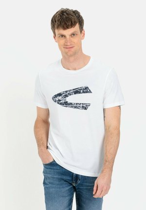 Hvid bomulds t-shirt med et tekstureret marineblåt grafisk design, der minder om et stiliseret bogstav eller form. Runde halsudskæring, korte ærmer.