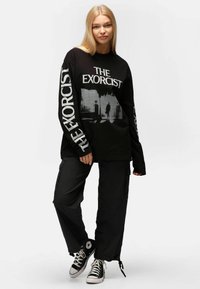 Svart långärmad skjorta med texten "THE EXORCIST" och ett framprintat grafiskt motiv. Matchas med svarta cargo-byxor och svarta sneakers.