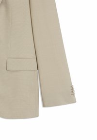 Beige blazer med strukturvæv, skræddersyet pasform, enkelt brystlomme og knappede manchetter med tre knapper.