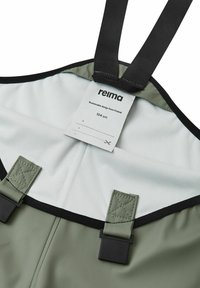 Grüne wasserdichte Overalls mit schwarzen verstellbaren Trägern, ausgestattet mit einem weißen Innenfutter und einem Etikett, das ein nachhaltiges Design aus Finnland anzeigt.