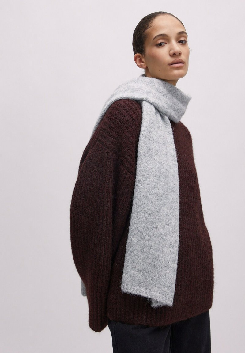 Gestrickter dunkelroter Pullover mit lockerer Passform, kombiniert mit einem hellgrauen Schal aus weichem Material, beides zusammen getragen für einen warmen Schichteffekt.